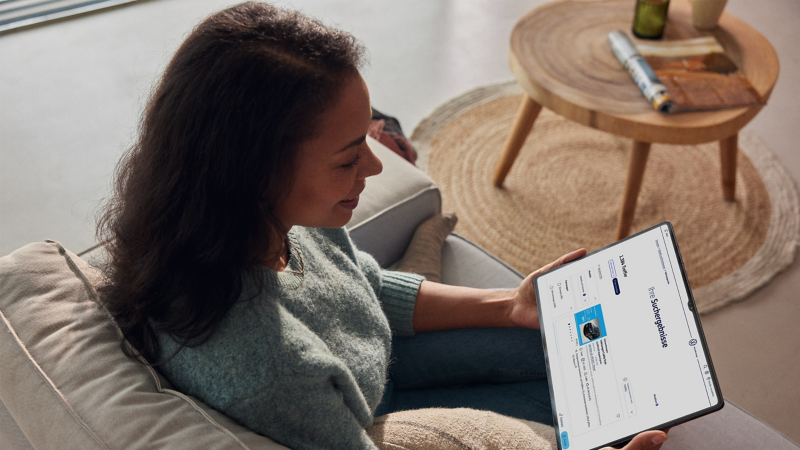 Eine Frau sitzt entspannt auf einem Sofa und schaut auf ein Tablet, das eine Suchergebnisseite mit einem Volkswagen-Angebot anzeigt.