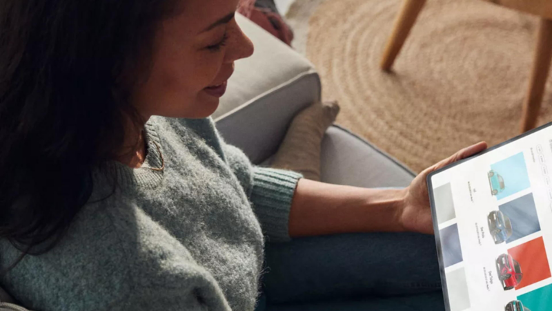 Frau sitzt auf einem Sofa und hält ein Tablet in der Hand, auf dessen Bildschirm der VW-Konfigurator zu sehen ist