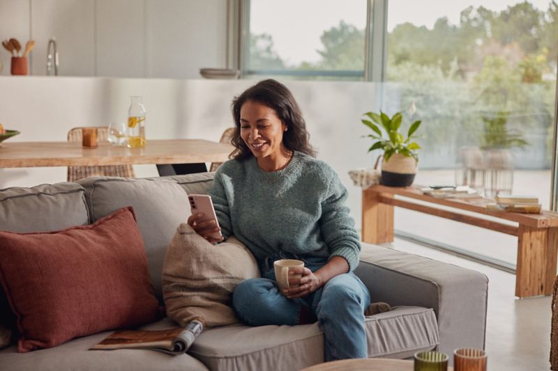 Eine Frau sitzt auf dem Sofa und schaut auf ein Mobiltelefon.