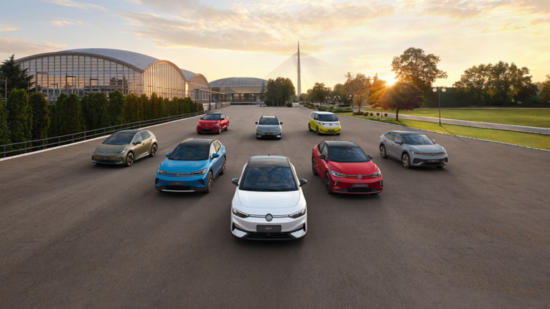 Alle VW ID-Modelle stehen auf einer breiten Straße vor einem modernen Gebäude bei Sonnenuntergang.