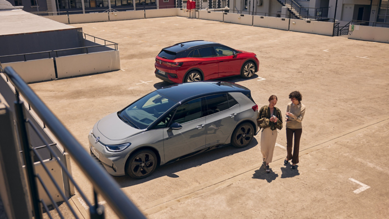 Ein VW ID.3 GTX und ein VW ID.4 GTX stehen auf einem Parkdeck, zwei Frauen gehen zum Ausgang.