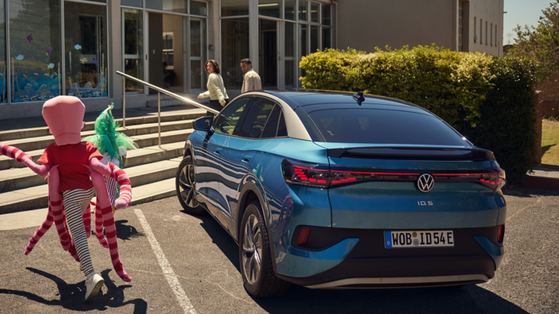 Blauer VW ID.5 in Heckansicht parkt vor einem Museum, zwei verkleidete Kinder rennen daneben zu ihren Eltern.