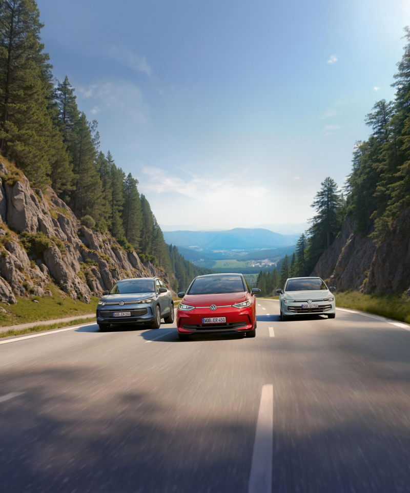 Three Volkswagen cars are driving between the mountains on a road.
