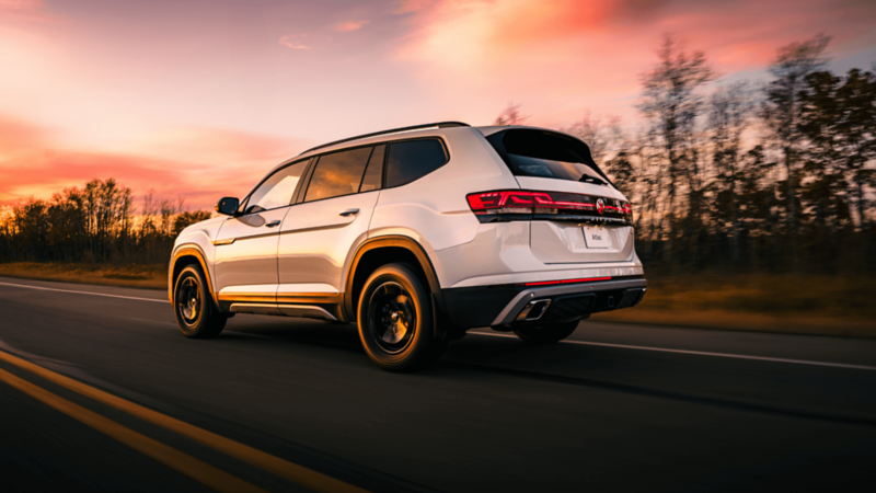 Rear-side view of a white Volkswagen Atlas driving on an open road at sunset, highlighting its 4MOTION all-wheel drive capability 