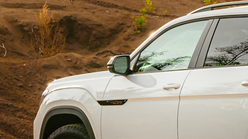 A red VW Atlas 2025 showcases its exterior mirror, equipped with heated, power-autofolding, memory, and reverse tilt-down features.