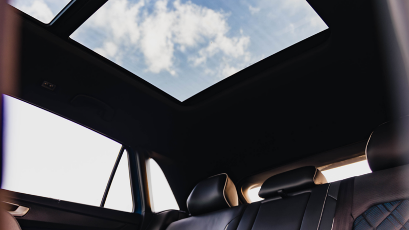 Interior view of the Volkswagen Atlas Cross Sport showing the rear seats and open panoramic sunroof with a clear sky above 