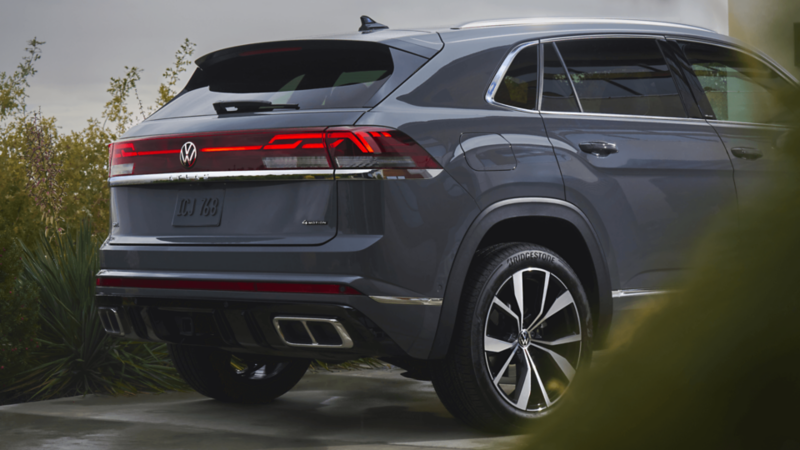 Rear-side view of a grey Volkswagen Atlas Cross Sport showing the tailgate, LED light strip, and dual exhaust tips 