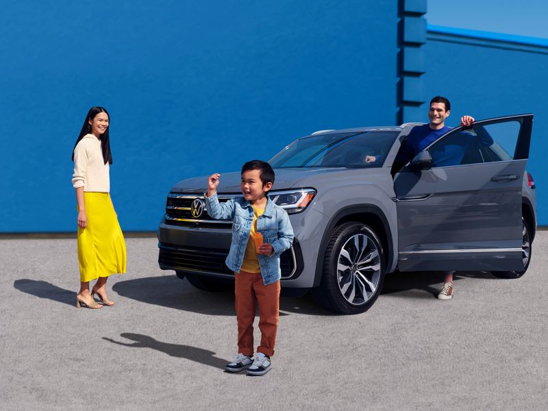 Une famille de trois personnes est à côté de son Cross Sport gris platine, devant un bâtiment bleu.