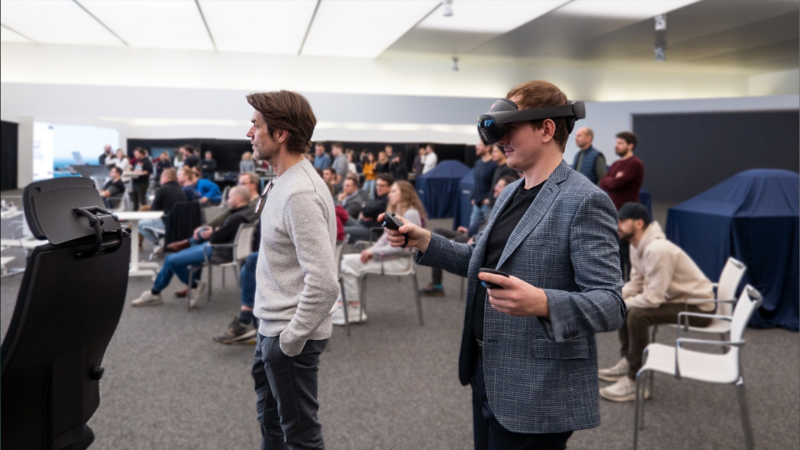Mann mit VR Brille steht in einem großen Raum mit vielen Menschen