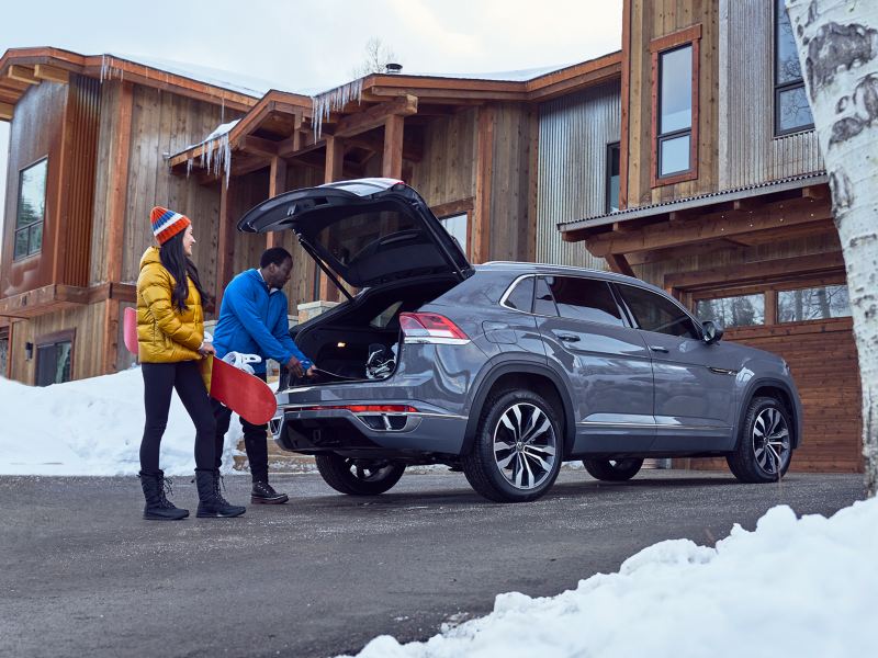 We see a man and woman loading up their snowboards in a grey Cross Sport parked on a chalet driveway.
