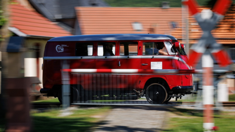 Der als Draisine umgebaute VW T1 an einer Bahnschranke vorbeifahrend.
