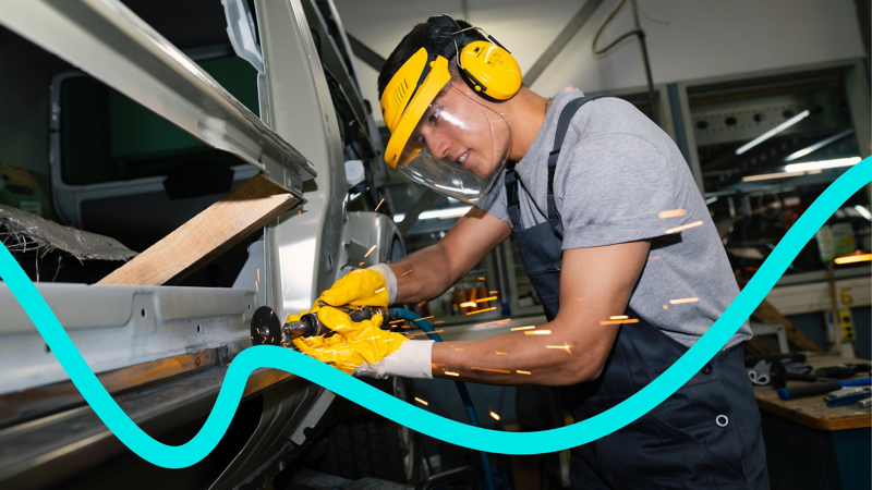 Junger Auszubildender mit blauer Latzhose bearbeitet den Schweller eines VW Touareg.
