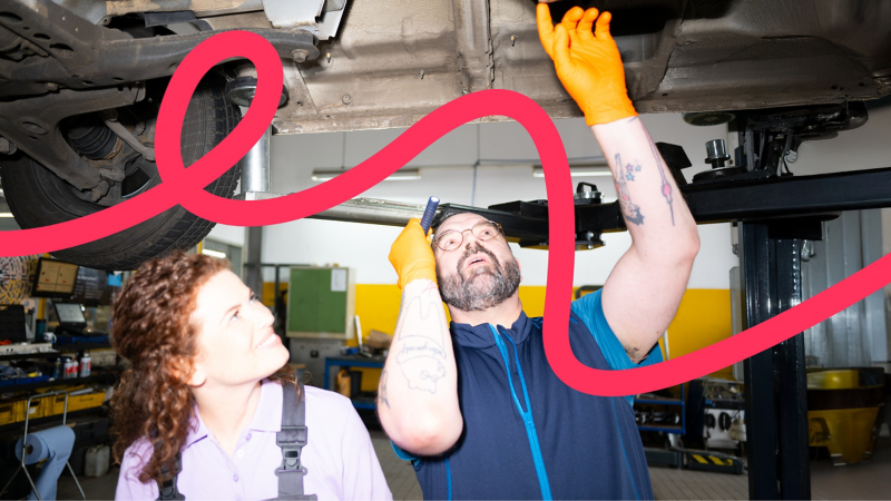 Ein Kfz-Mechatroniker und eine Kfz-Mechatronikerin untersuchen den Unterboden eines Volkswagen Nutzfahrzeugs.