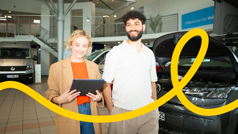 Zwei Mitarbeitende stehen in der Werkstatt neben einem geöffneten Volkswagen Nutzfahrzeug und lächeln.