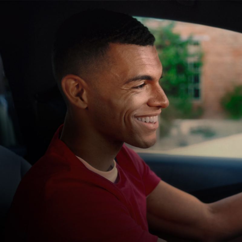 A smiling young man driving a VW, outgoing link to volkswagenplus.ca/en