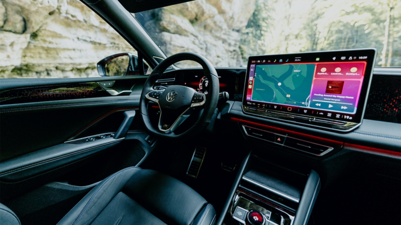 Intérieur de la Volkswagen Tiguan avec tableau de bord et deux grands écrans numériques. Le volant et le siège conducteur en cuir noir avec des coutures bleues sont visibles.