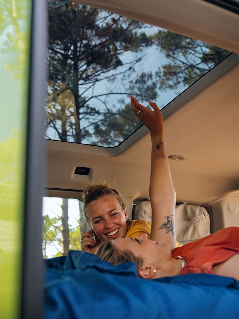 VW California vue intérieure avec toit panoramique dans la forêt 2 femme sur la couchette