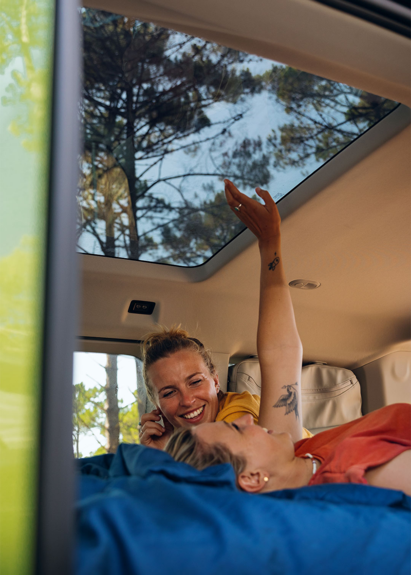 VW California vue intérieure avec toit panoramique dans la forêt 2 femme sur la couchette