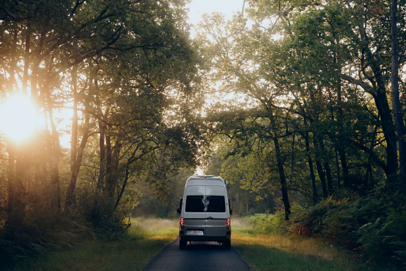 vue d'arrière du Grand California VW avec couché de soleil dans une forêt