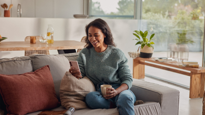 A person sitting on the sofa and looking at a mobile phone, smiling