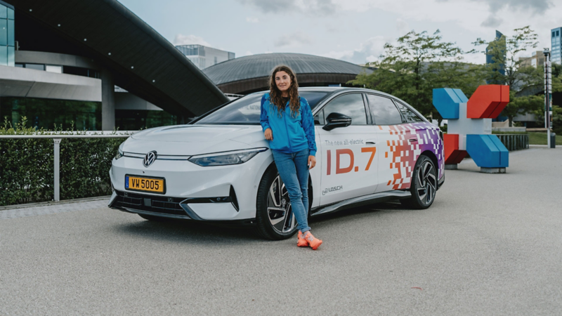 Une femme chaussée de baskets orange est appuyée sur le côté du capot d'une ID.7 blanche.