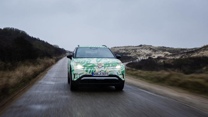 Ein VW ID. Cross mit Konzeptbeklebung fährt auf einem Küstenlandweg durch Dünen. 