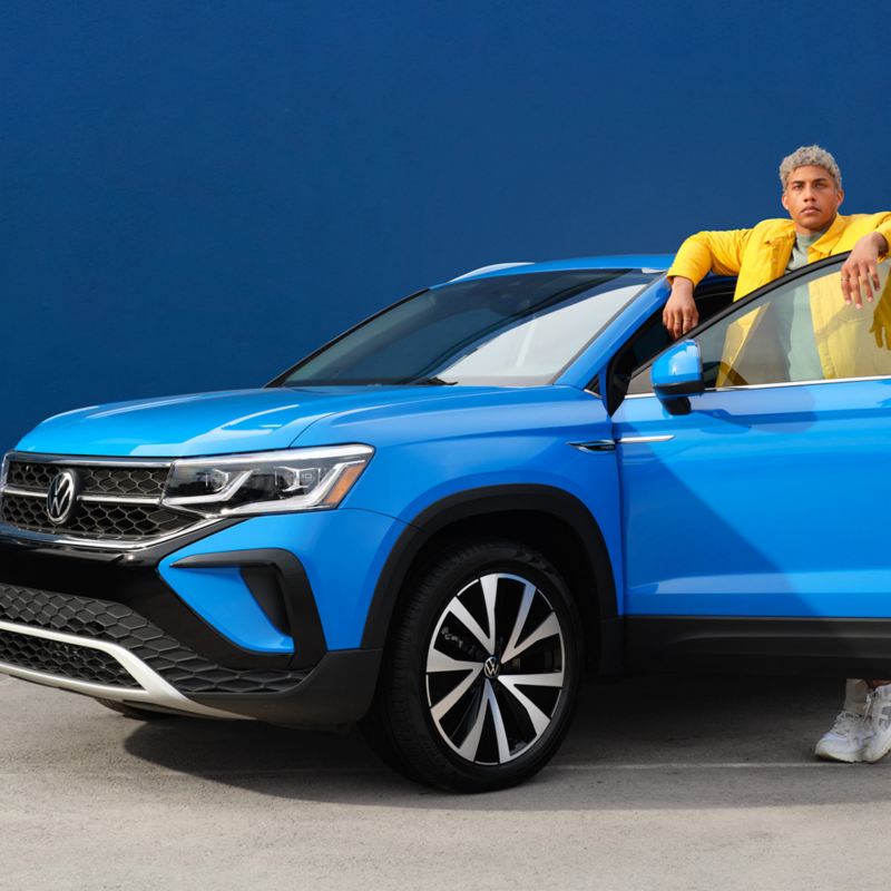 Un homme se tient derrière la portière ouverte d’un Taos de Volkswagen bleu métallisé, lien vers la page vehicules-neufs