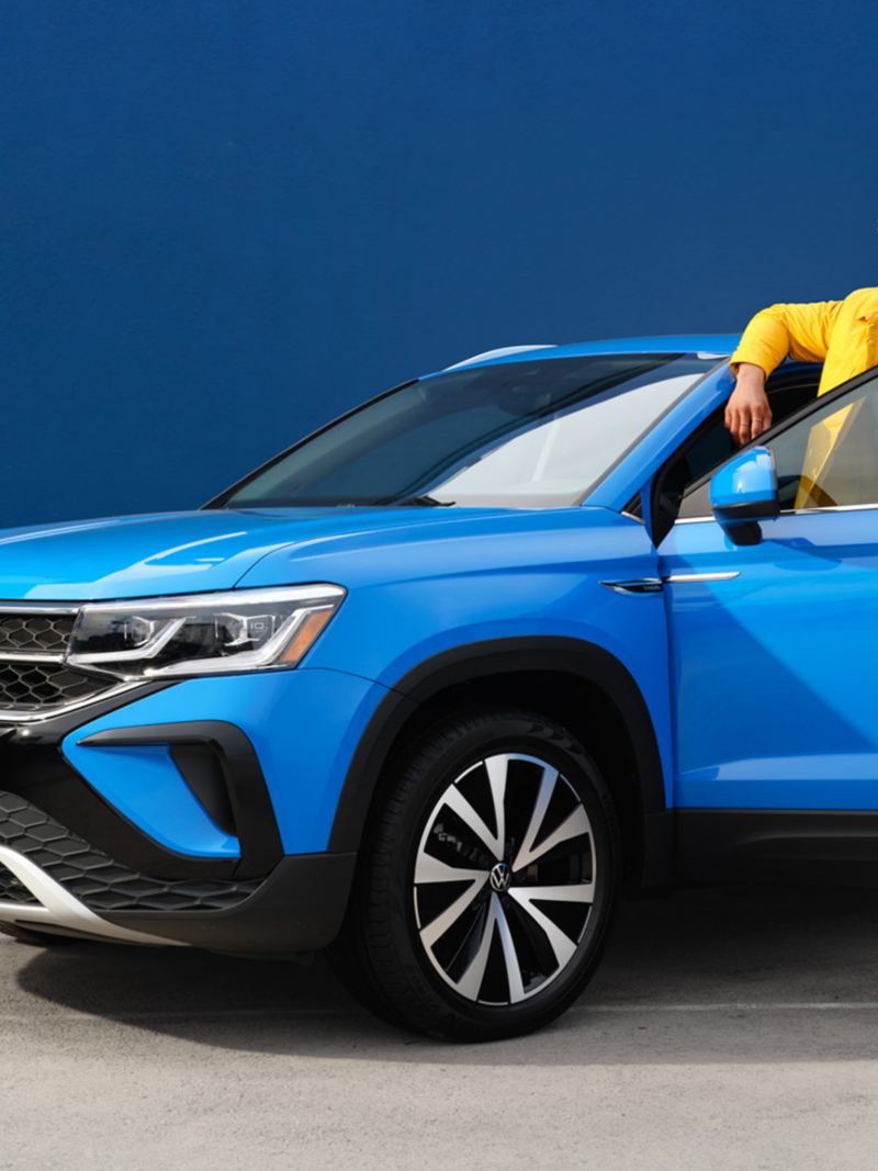 Un homme se tient derrière la portière ouverte d’un Taos de Volkswagen bleu métallisé., lien vers la page vehicules-neufs