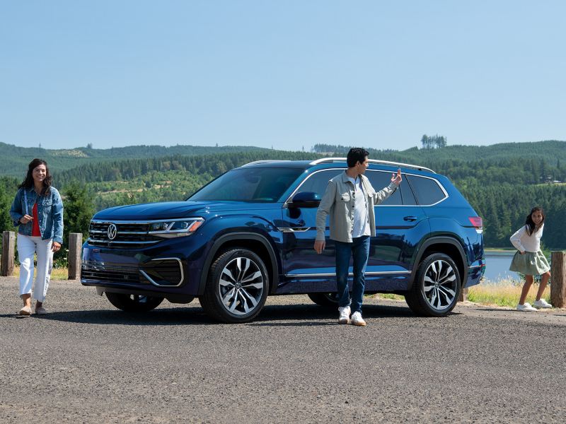 We see a man, woman and three children walking close to a blue Atlas on a sunny day.