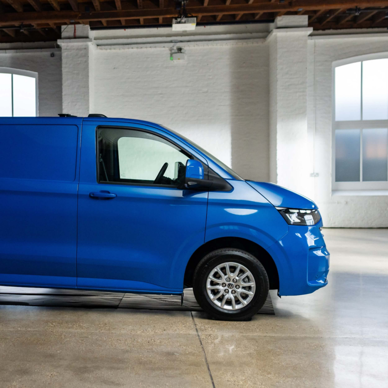 Partial side view of a blue Transporter panel van parked in a cream room