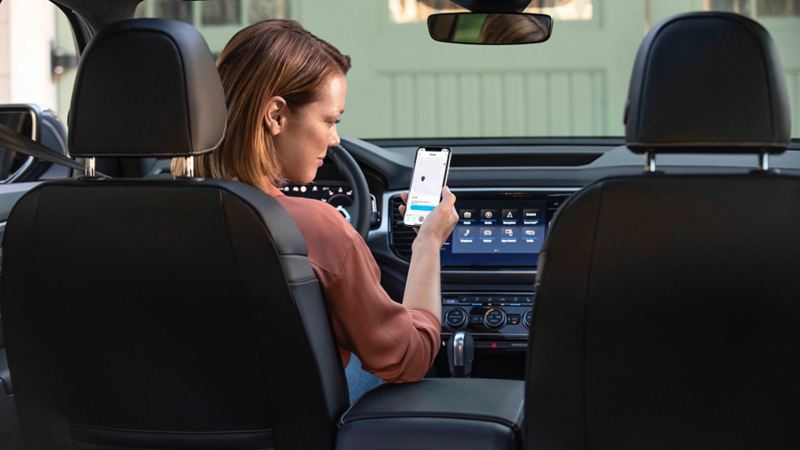 Woman sitting in a VW car and looking at the Car-Net® app
