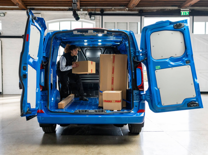 Open rear of blue Volkswagen Transporter van showing cargo space with boxes being loaded.