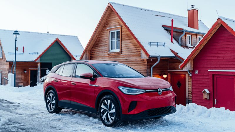 A bright red Volkswagen SUV is parked in front of a wooden house with a snow-covered roof
