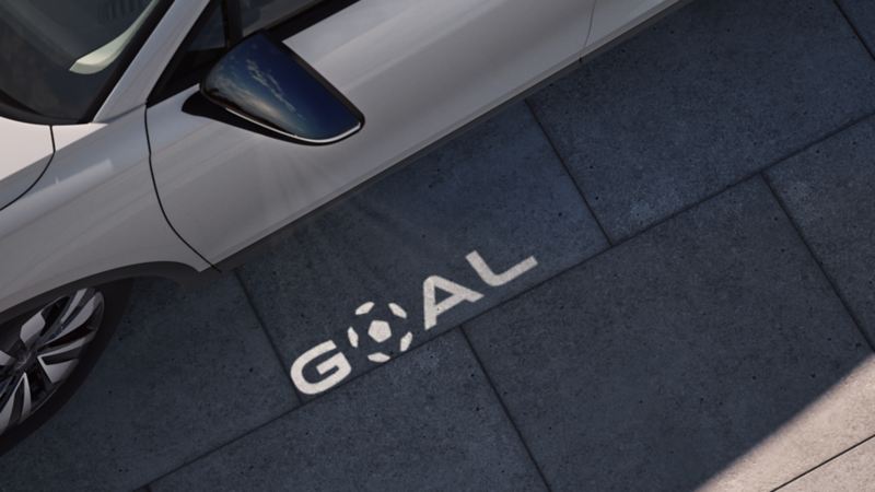 Ein GOAL Logo wird auf den Boden neben der Fahrertür eines VW Tiguan GOAL projiziert.