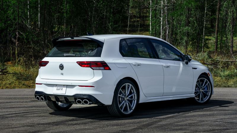A side view of a white 2024 Volkswagen Golf R parked on a road with lush greenery in the background.