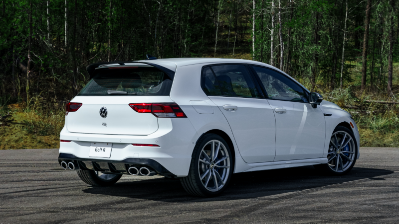 Vue latérale d'une Volkswagen Golf R 2024 blanche garée sur une route avec une végétation luxuriante en arrière-plan.