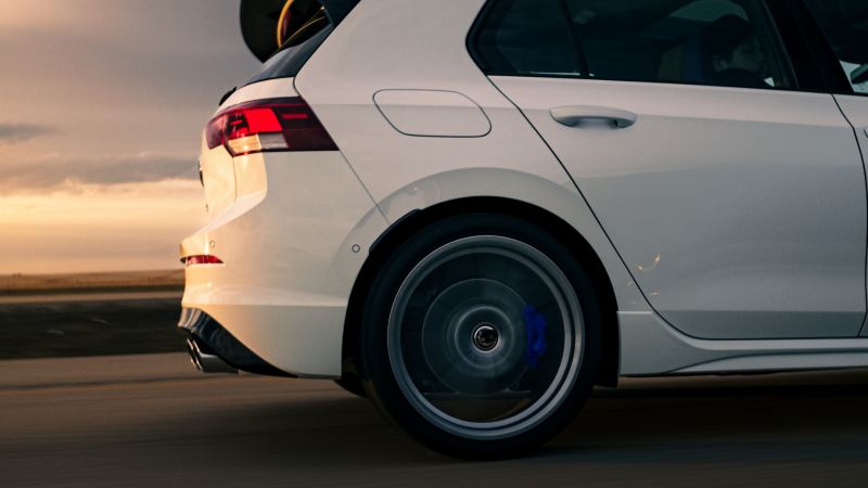 The rear wheel of a white 2024 Volkswagen Golf R spinning as it drives down a road.