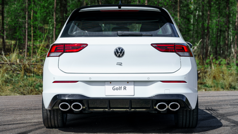 Vue arrière d'une Volkswagen Golf R 2024 blanche garée sur une route avec une végétation luxuriante en arrière-plan.