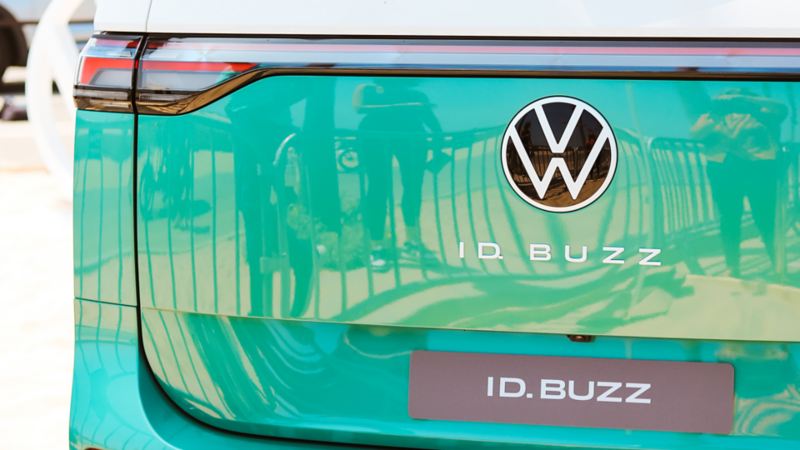Close-up of a two-tone white-green Volkswagen ID. Buzz’s rear section, featuring the distinctive VW logo and model name on a sleek design with reflections on the glossy surface