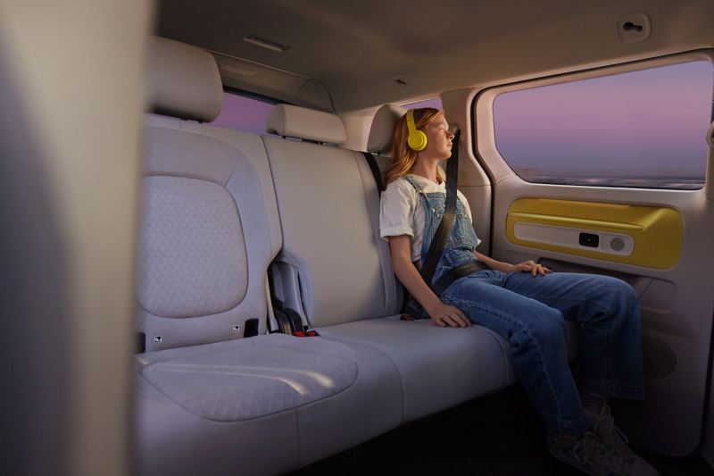 Une jeune femme assise sur la banquette arrière du Volkswagen ID. Buzz avec un casque jaune sur les oreilles