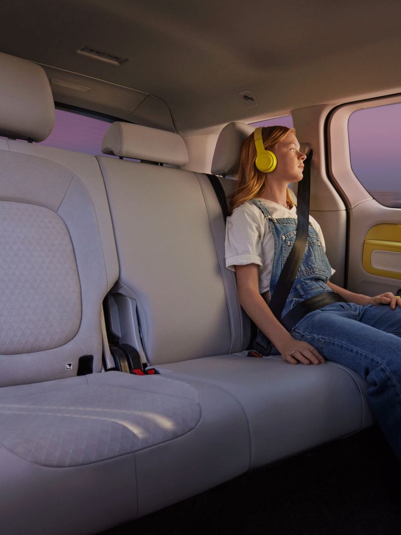Une jeune femme assise sur la banquette arrière du Volkswagen ID. Buzz avec un casque jaune sur les oreilles