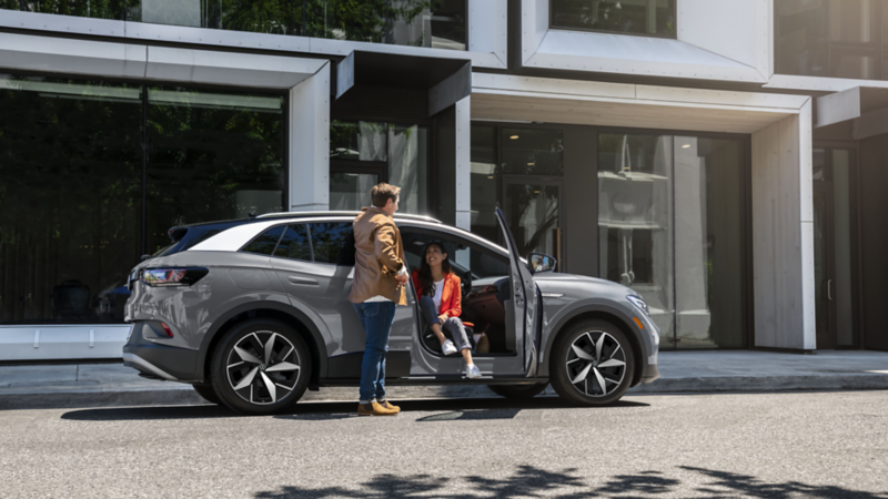 Homme parlant à une femme assise dans une Volkswagen ID.4 grise garée près d'une copropriété