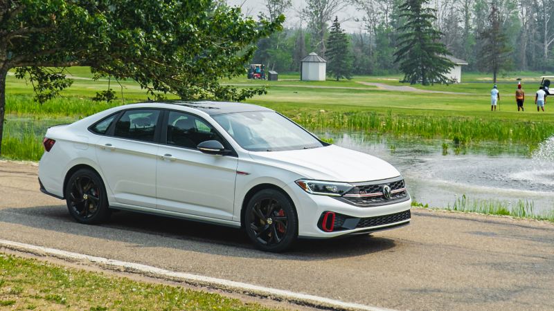 A white 2023 Volkswagen Jetta GLI parked on a road near a pond with a scenic view.