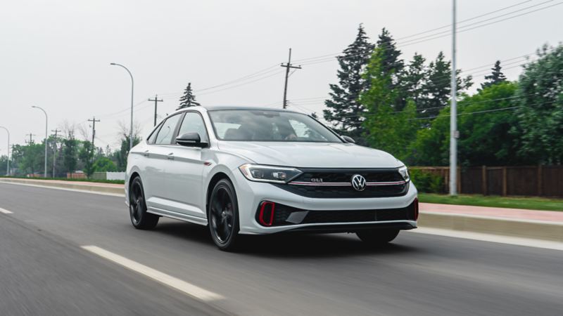 A white 2023 Volkswagen Jetta GLI cruising on the road, showcasing its sleek design and smooth ride