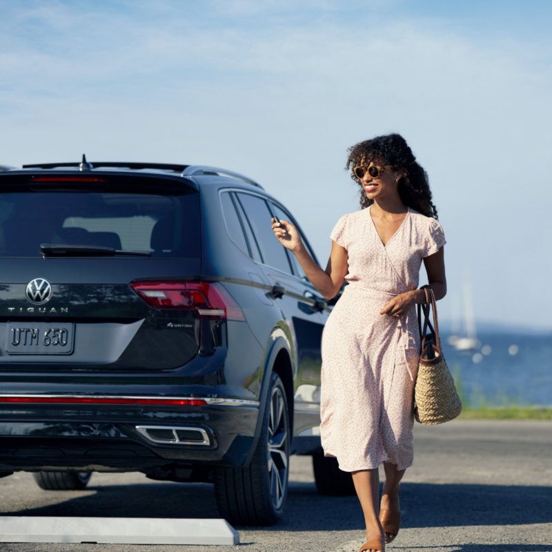 A woman wearing a sundress walking away from a vehicle while holding keys in her hand