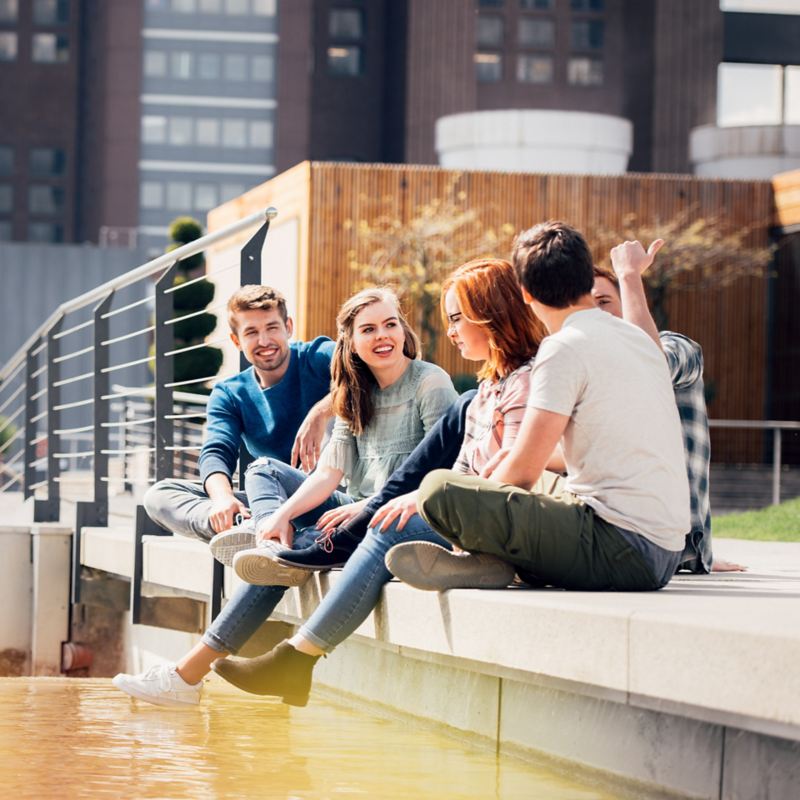 Fünf junge Menschen sitzen gemeinsam am Ufer eines Gewässers
