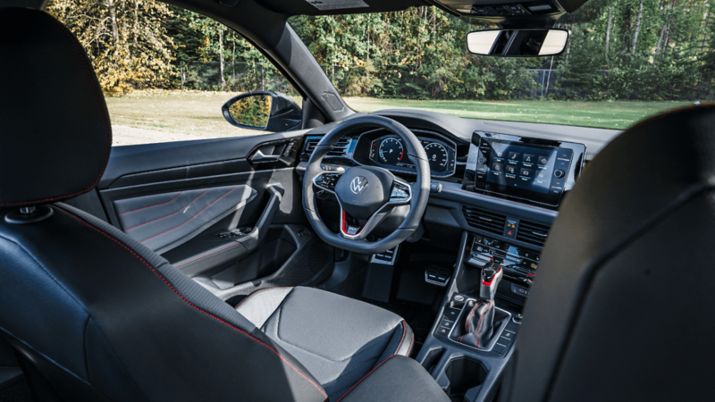 Interior view of the 2026 Jetta GLI showing the driver’s seat, leather steering wheel with red accents, and infotainment system.
