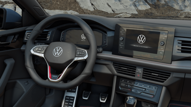 Interior view of the 2026 Jetta GLI showing the driver’s seat, leather steering wheel with red accents, and infotainment system.