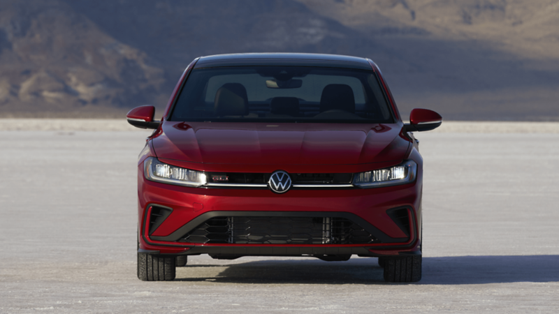 Front-facing view of the 2026 Jetta GLI in red, driving on open salt flats with a mountain backdrop