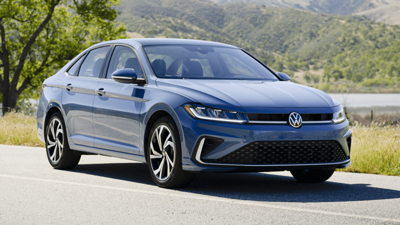 Front three-quarter view of the 2026 Volkswagen Jetta in blue, parked on a scenic roadside with hills in the background.